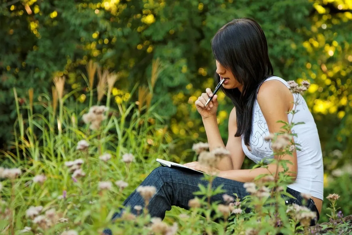 a young woman writing in her journal sitting on the grass