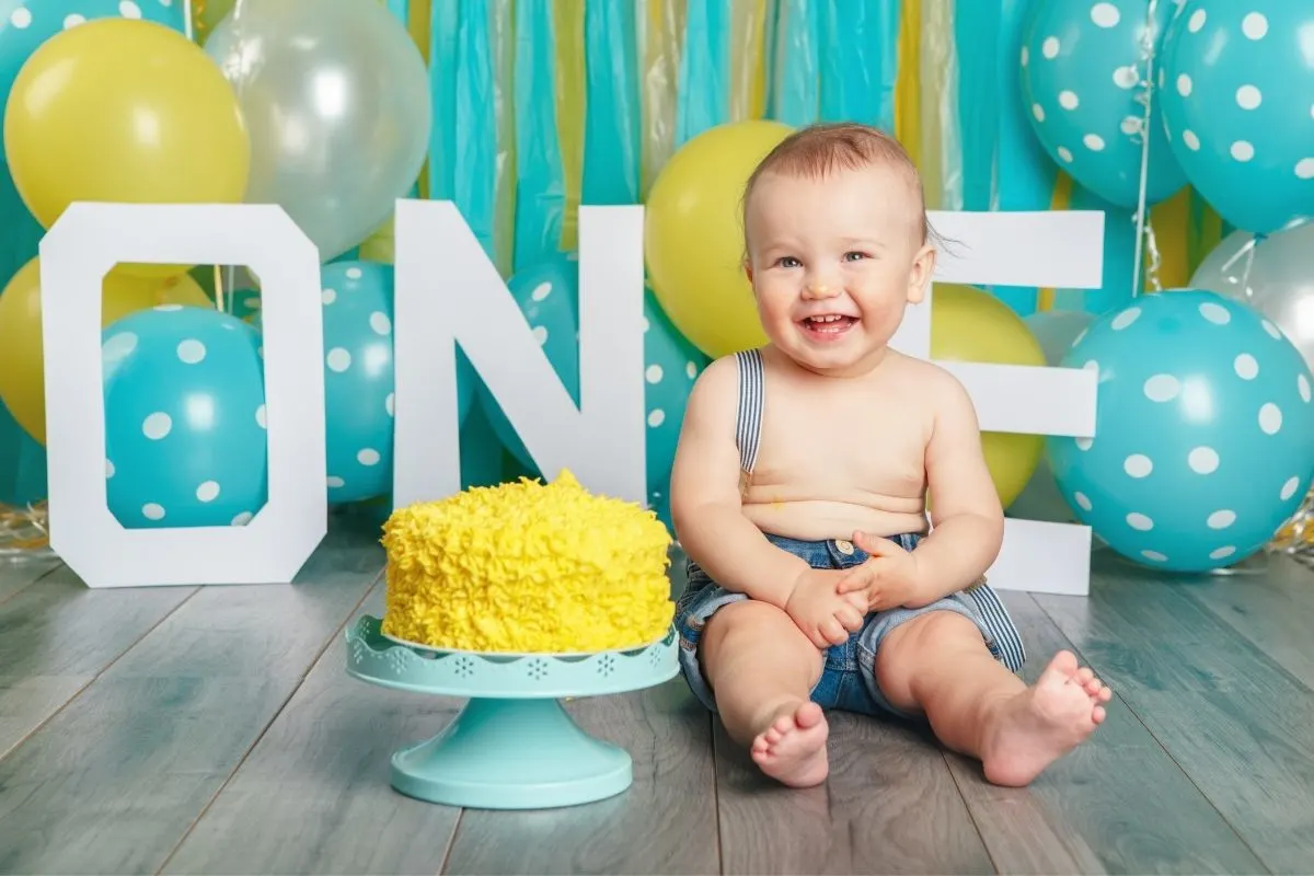 one year old boy in front of balloons and next to a cake