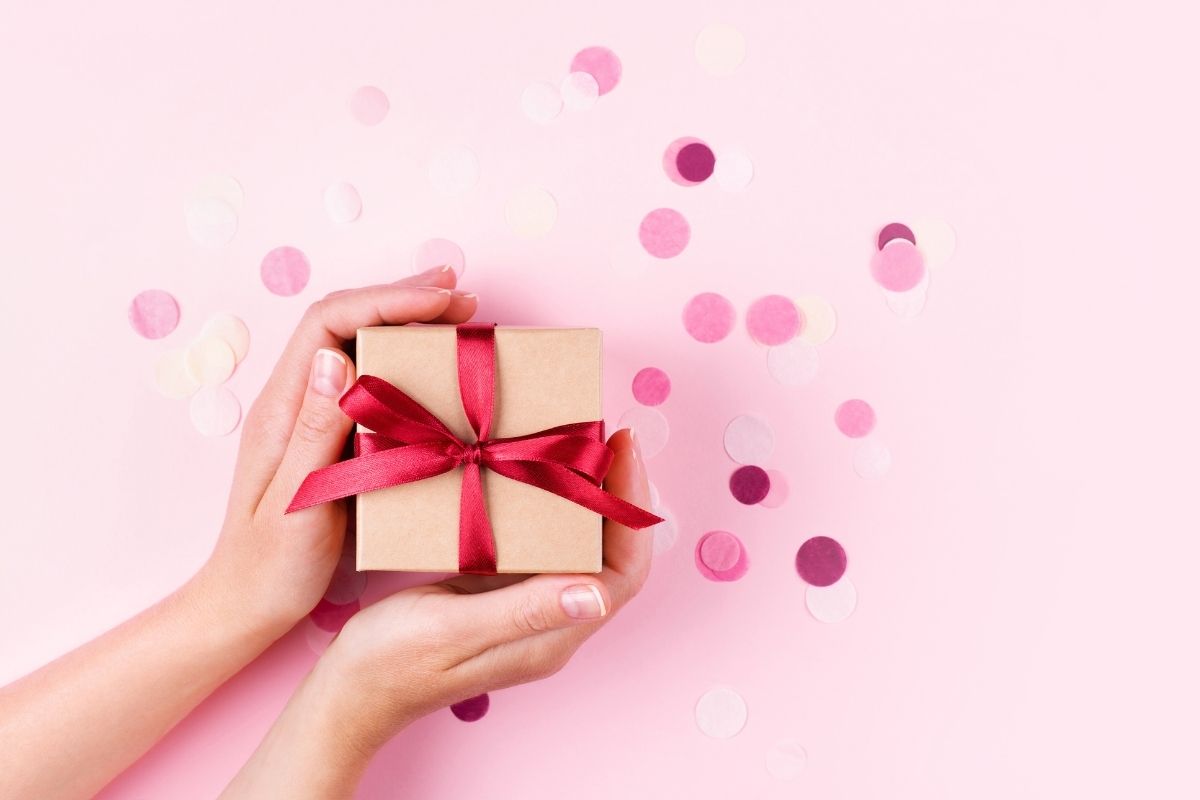 woman's hands holding a tan colored gift box with a red bow