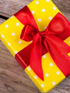 gift box wrapped in yellow polka dotted paper and a red bow
