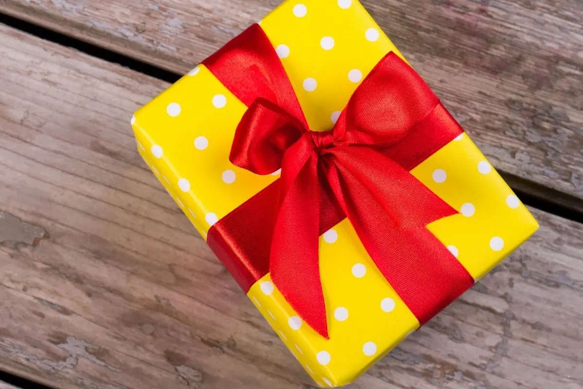 gift box wrapped in yellow polka dotted paper and a red bow